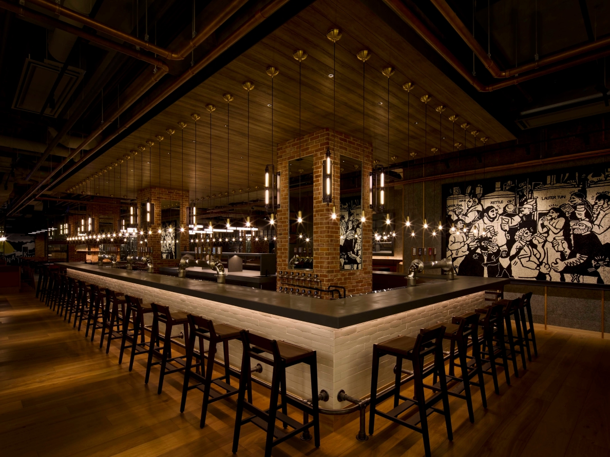 Bar counter with brick pillars and pendant lights at YONA YONA TOKYO BREWERY