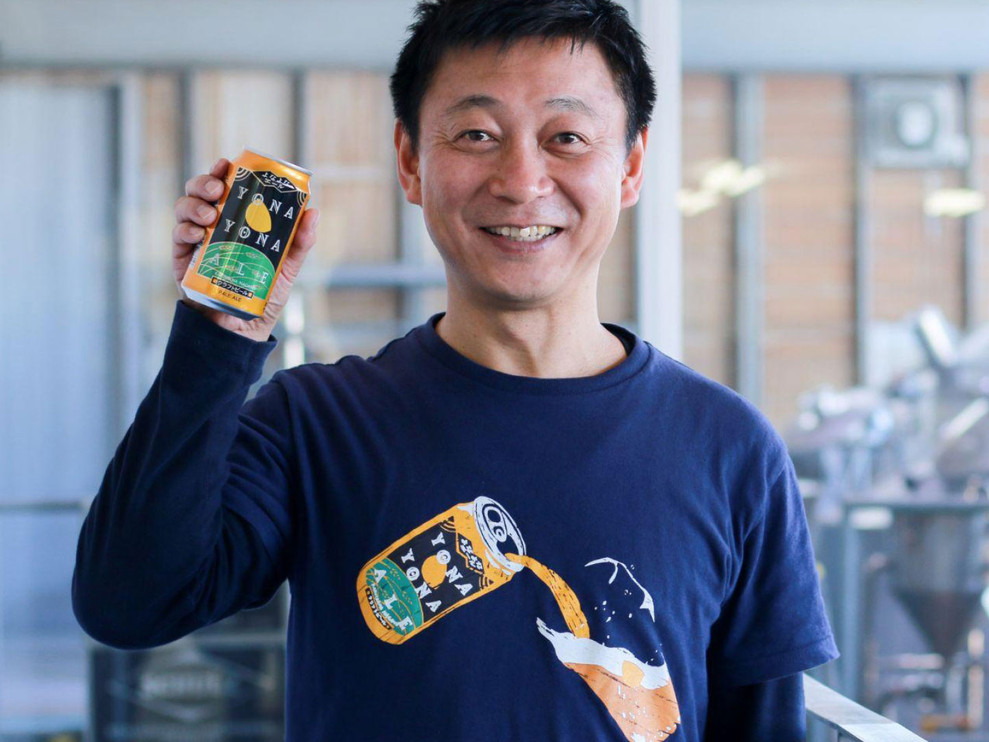 Naoyuki Ide (Tencho), President and CEO, smiling and holding a can of Yona Yona Ale with the brewery in the background