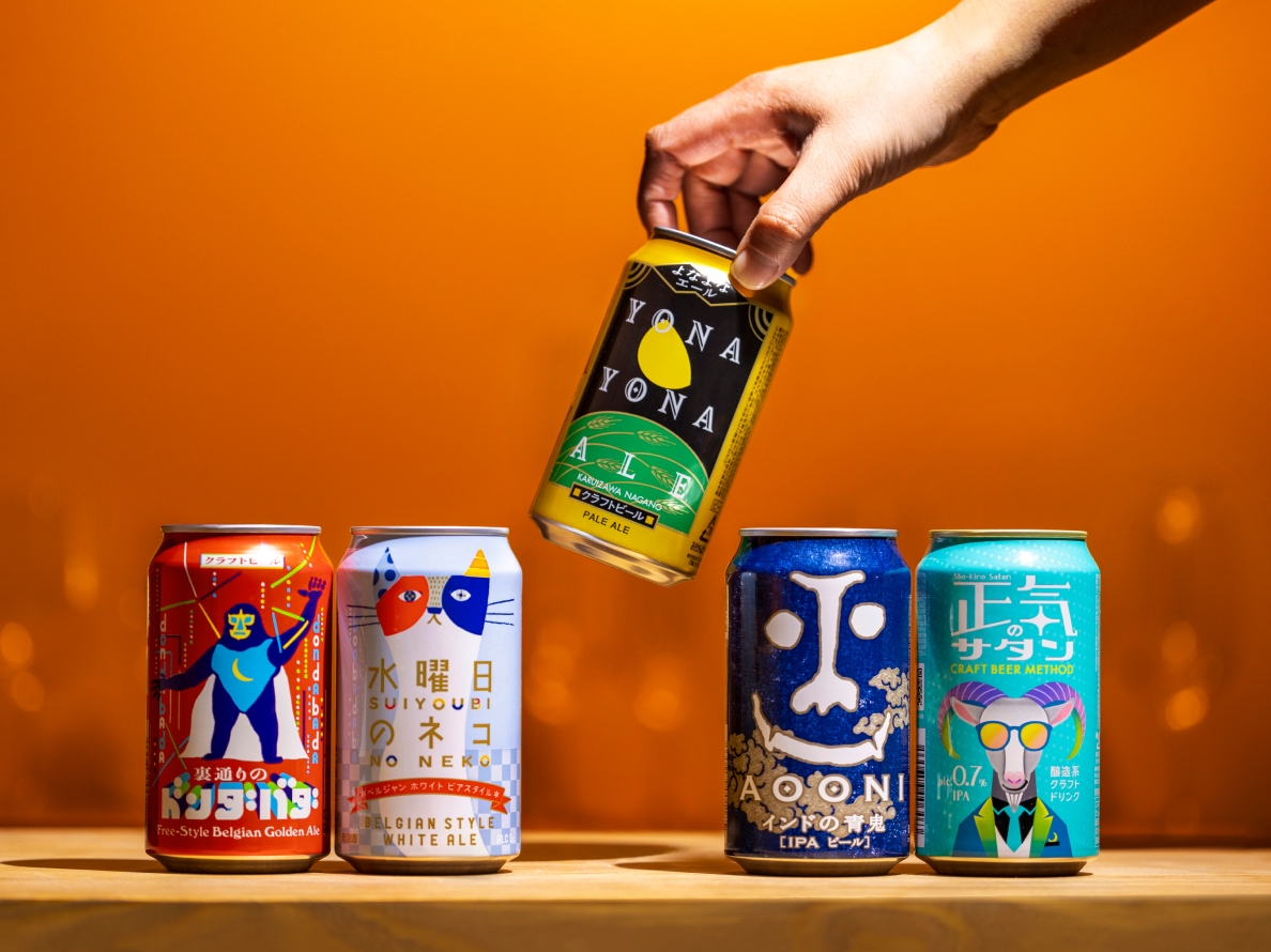 クラフトビールNo.1企業、左から「裏通りのドンダバタ」「水曜日のネコ」「よなよなエール」「インドの青鬼」「正気のサタン」5種類の缶が並んだ商品写真、真ん中の「よなよなエール」を手に取っている